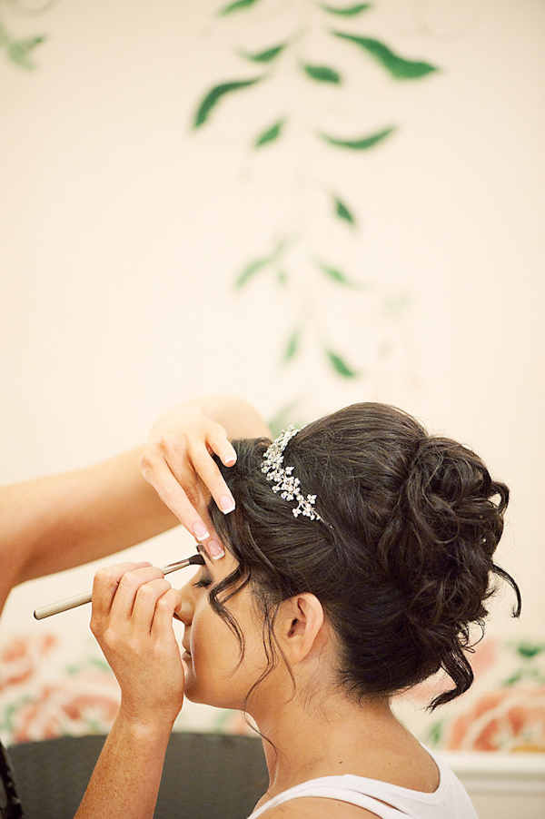 the beautiful bride with a loose updo and white floral hair accessory having her makeup applied - photo by Houston based wedding photographer Adam Nyholt 